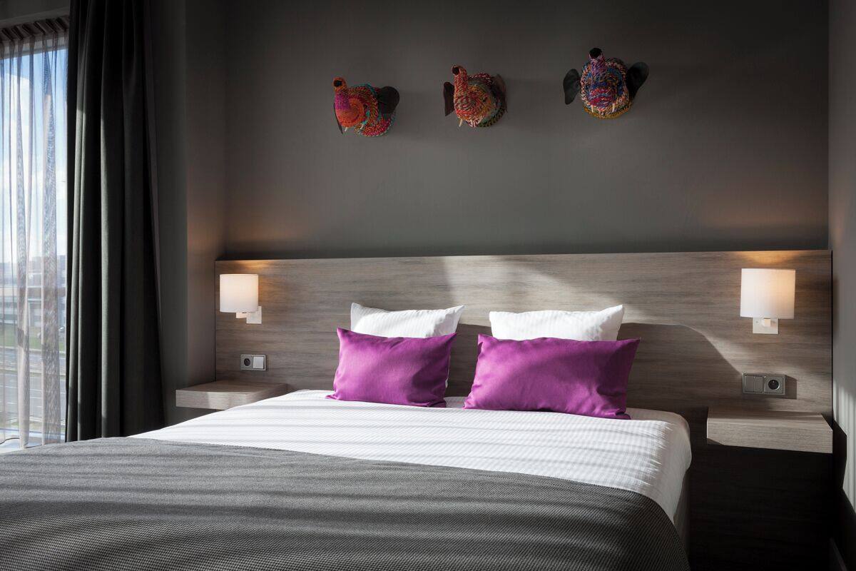 Una habitación de hotel moderna con una cama grande, dos lámparas fijadas a la pared y decoración mural.