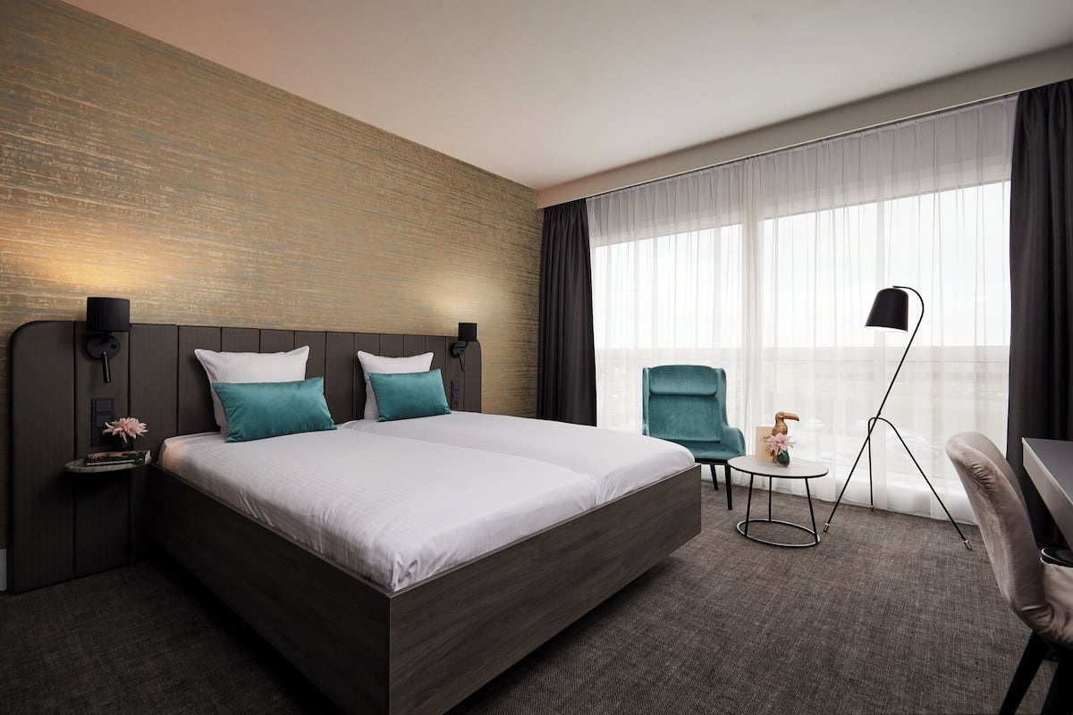 Habitación de hotel moderna con una cama grande, un escritorio, una silla y vistas al exterior.