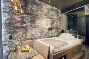 A modern bedroom with a large bed, a seating area with a table, and a wall-mounted light fixture.