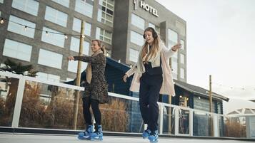 Dos personas patinando frente a un hotel con diseño moderno y amplias ventanas.