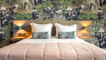 A hotel room with a large bed, two white pillows, a patterned pillow, and a headboard with wall-mounted lights.
