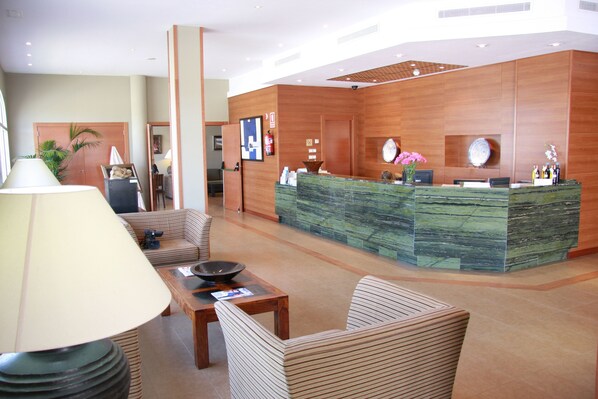 A reception area with a wooden reception desk, seating area with chairs, a table, and a lamp.