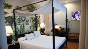 A four-poster bed with white linens, a nightstand with a lamp, a wall-mounted TV, and a wooden bench. - Cortijo Chico Málaga Airport (Alhaurin de la Torre)