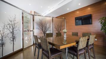 Una sala de reuniones moderna con una mesa de vidrio, sillas de madera y un televisor montado.
