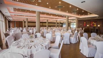 Un amplio salón de banquetes con mesas redondas dispuestas para cenar, sillas blancas y un diseño de techo moderno.