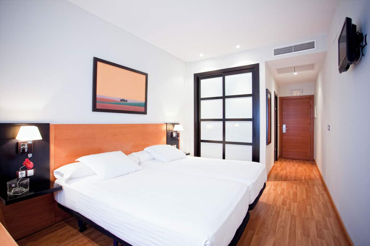 A hotel room with a large bed, a nightstand with a lamp, a painting on the wall, and a wooden floor.