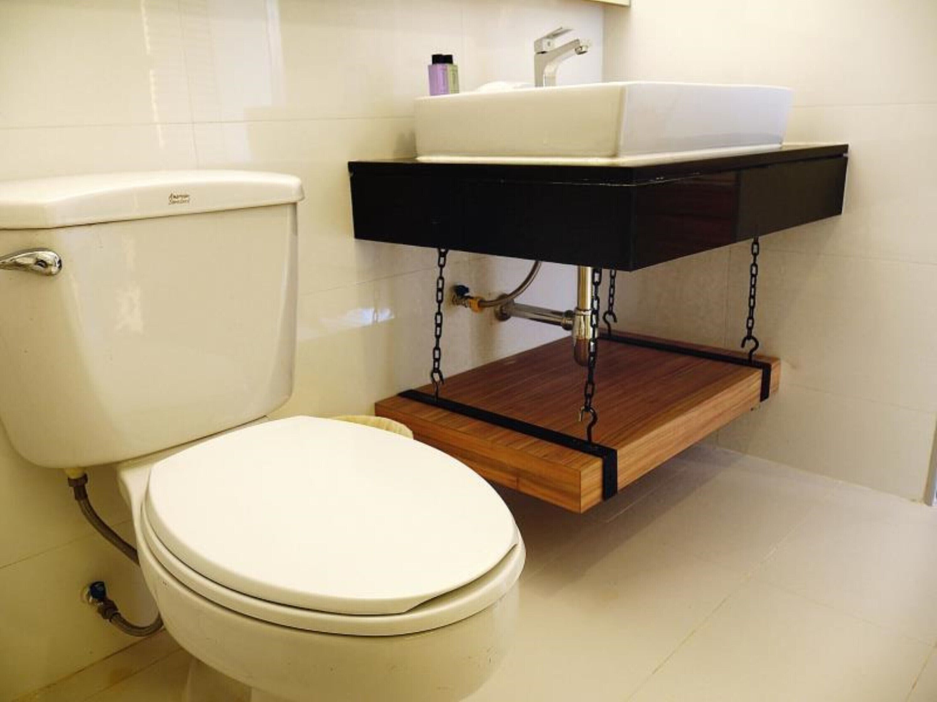 Eine Toilette mit einem Holzregal darüber, einem weißen Waschbecken und einem Toilettenpapierhalter.