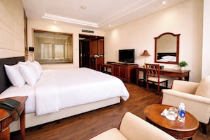 A hotel room with a large bed, a desk with a computer, a chair, a small table with a lamp, and a mirror. - Saigon Halong Hotel (Bai Chay)