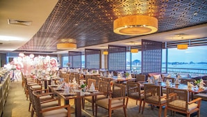 A restaurant with a view of the sea, featuring wooden tables and chairs, patterned ceiling, and decorative lighting. - Saigon Halong Hotel (Bai Chay)