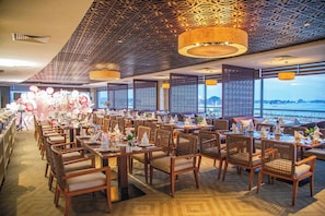 A restaurant with a view of the sea, featuring wooden tables and chairs, patterned ceiling, and decorative lighting. - Saigon Halong Hotel (Bai Chay)