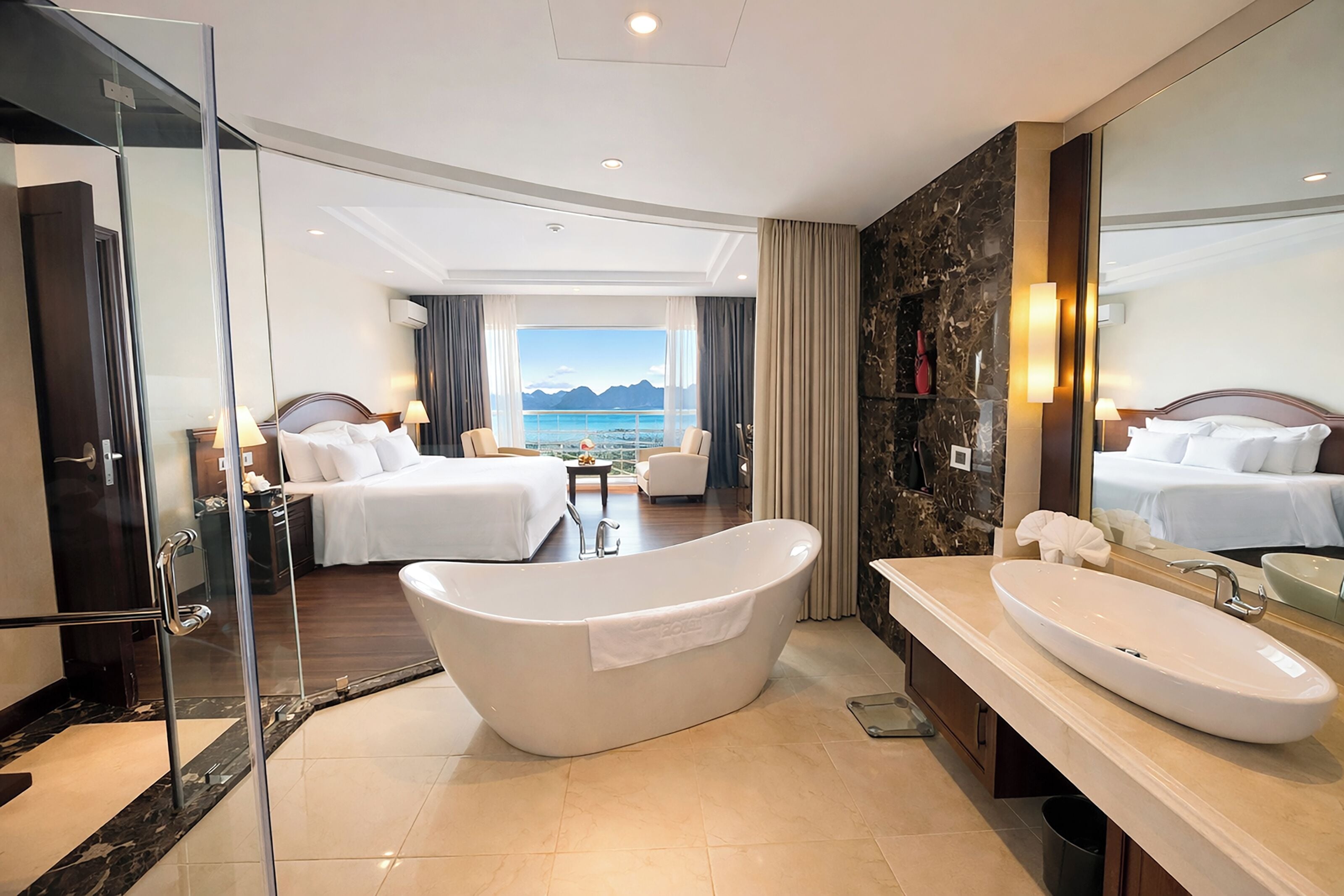 Une chambre d’hôtel moderne dotée d’une grande baignoire, d’un lit double, d’un canapé et offrant une vue sur la mer.