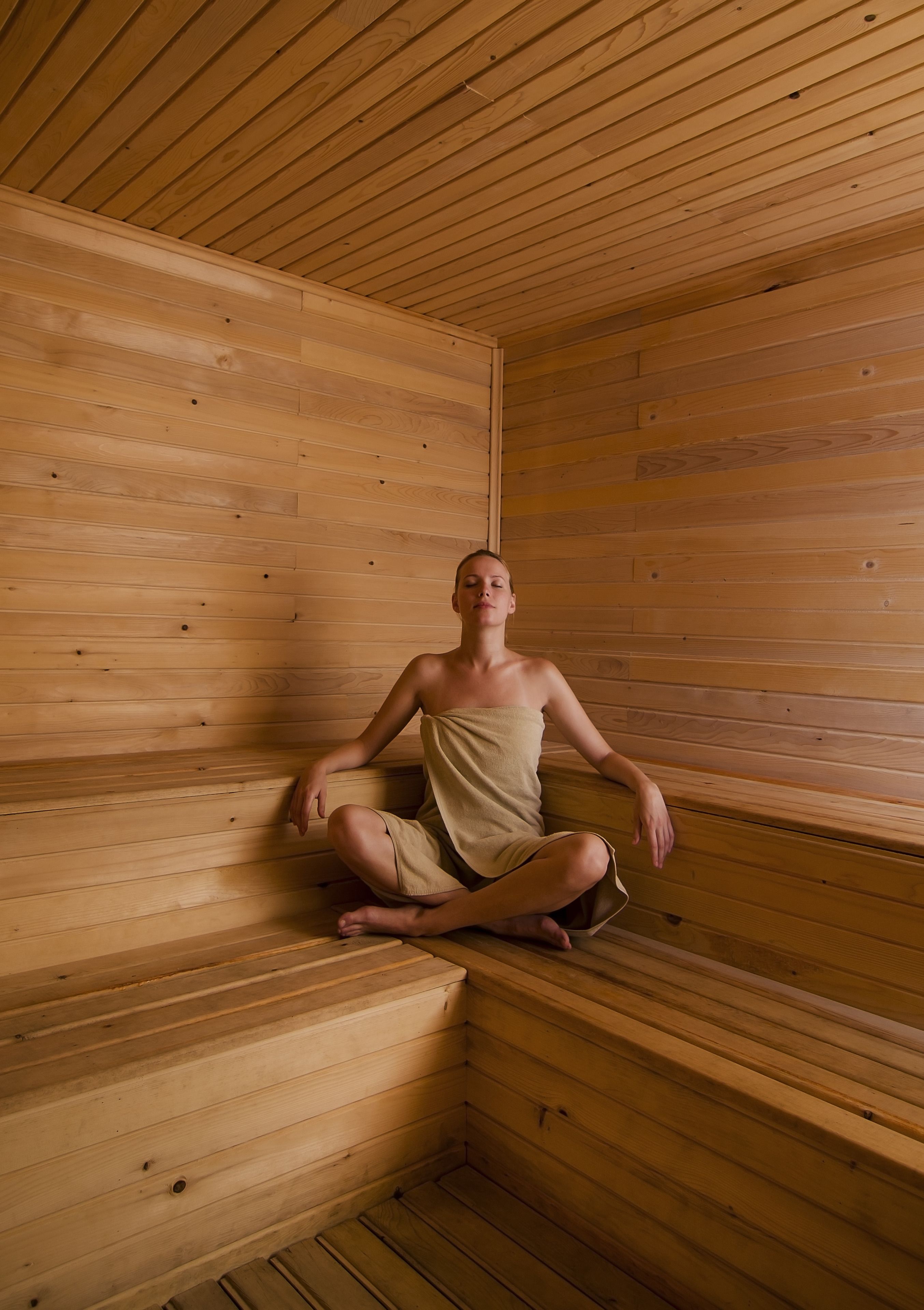 Una persona sentada en una sauna de madera con bancos y techo inclinado.