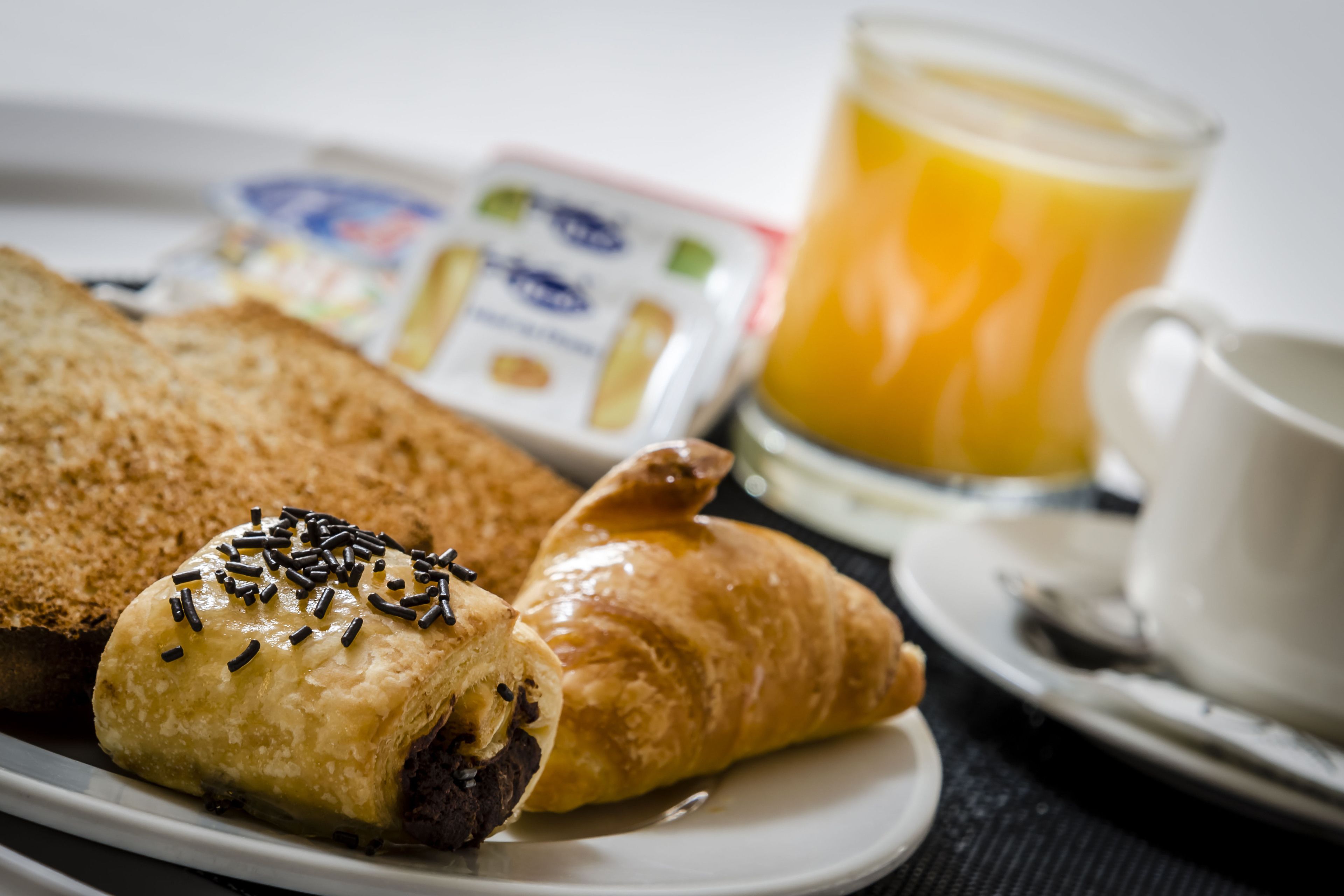 Ein Teller mit Frühstück, darunter ein Croissant, Brot, ein Glas Orangensaft und eine Tasse Kaffee.
