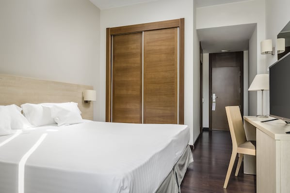 A hotel room with a large bed, a wooden wardrobe, a desk with a chair, and a desk lamp. - Exe Barcelona Gate (Sant Joan Despi)