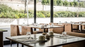 Un restaurante con mesas preparadas para comer, mostrando una vista de vegetación y edificios al fondo.