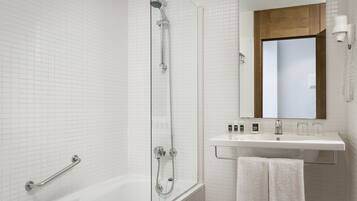 Un baño moderno con ducha de vidrio, una bañera blanca, tocador con espejo y perchero para toallas.