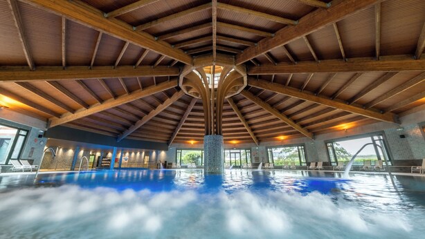 An indoor swimming pool with a high wooden ceiling and a central pillar.