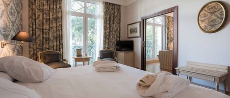 A hotel room with a large bed, a chair, a small table, a TV, and a mirror.