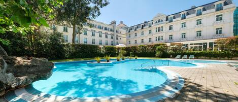 Une piscine dotée d’une terrasse carrelée, entourée d’un bâtiment comportant de nombreuses fenêtres et des balcons.