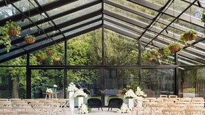 A greenhouse venue with rows of chairs, hanging planters, and a central floral arrangement.