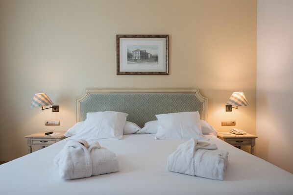 A neatly made bed with white linens and two towels, a framed picture on the wall, and two bedside lamps.