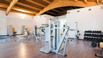 Un gimnasio con diversas máquinas de ejercicio, bancos y un estante con mancuernas.