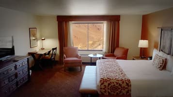 A hotel room with a bed, a desk, a chair, a TV, and a window with curtains.