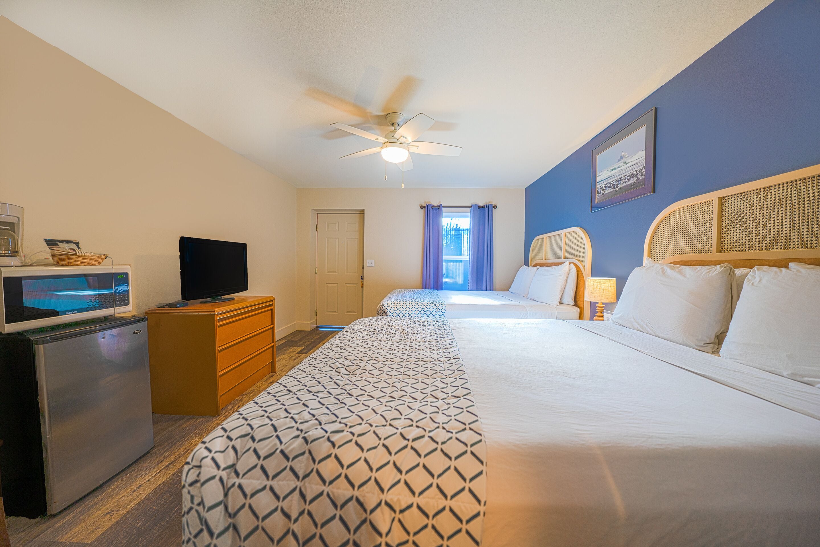 A hotel room with a bed, a television, a refrigerator, a desk, and a ceiling fan.