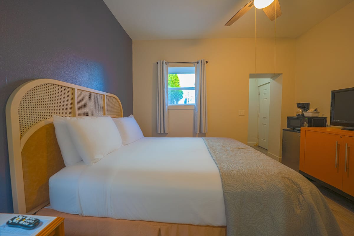 Una camera d'albergo con un letto, una televisione, un piccolo mobile e una finestra con tende.