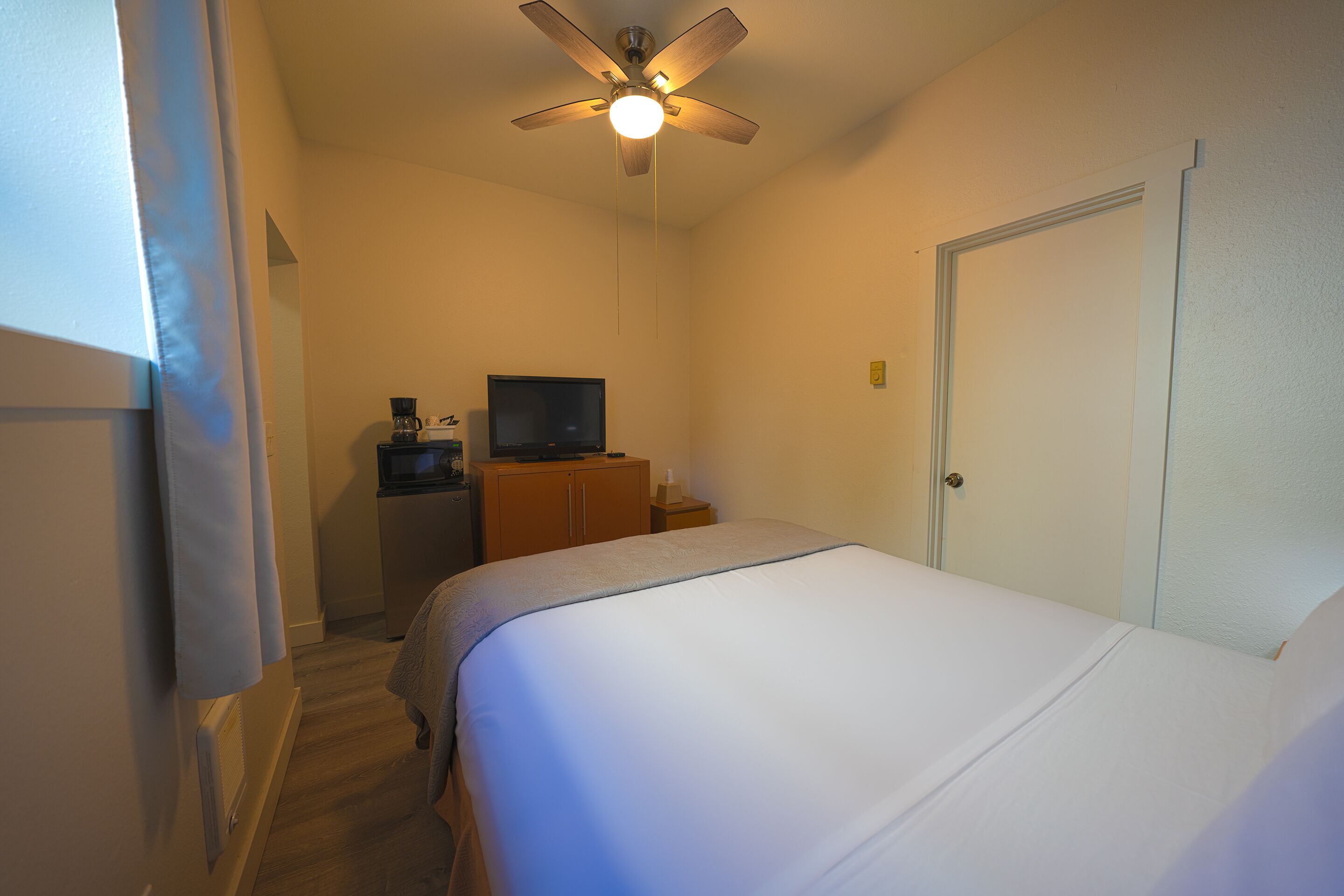 A hotel room with a bed, a television on a wooden cabinet, and a ceiling fan.