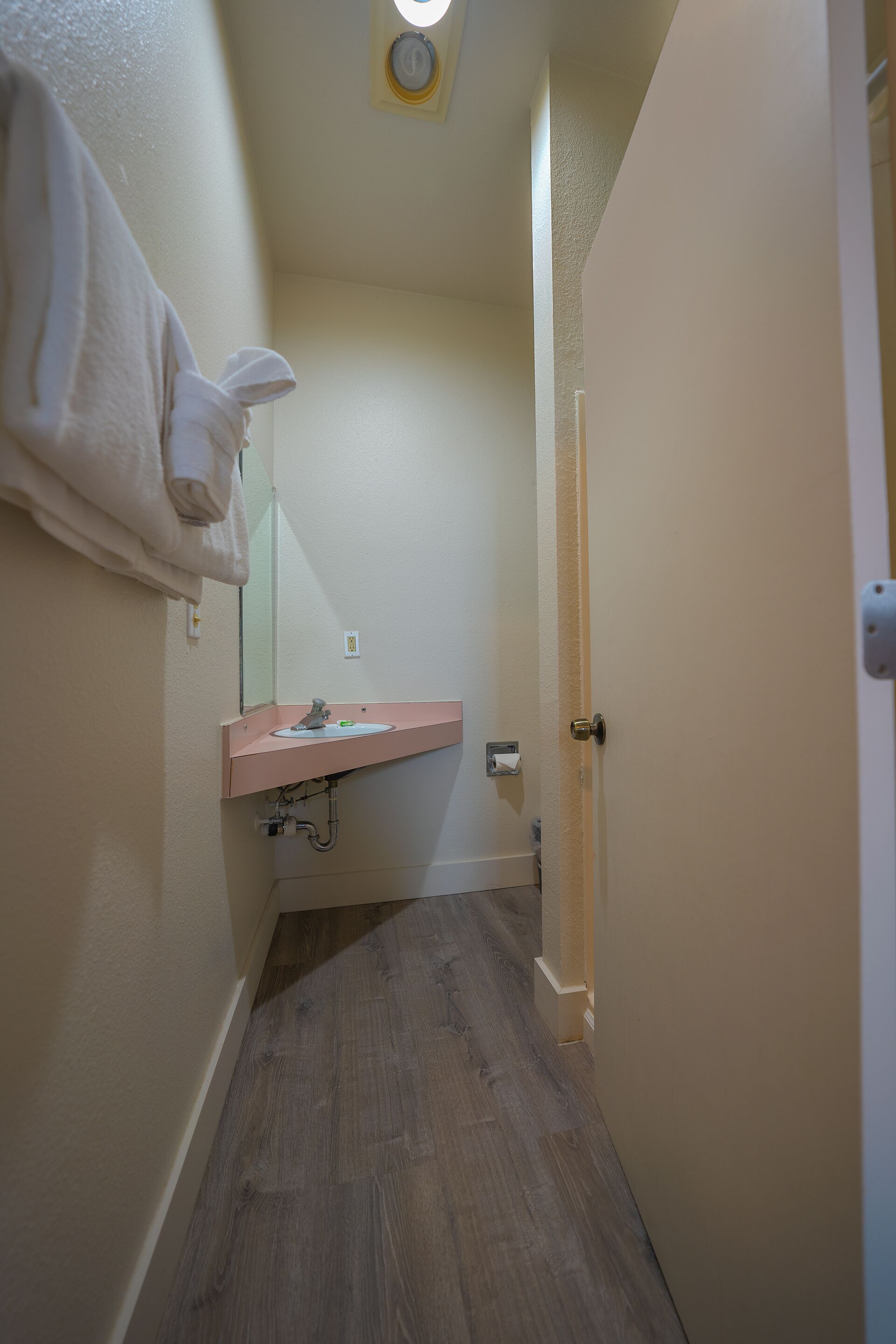 A narrow hallway with a bathroom featuring a sink, mirror, and towel hanging on the wall.