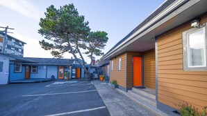 Un motel con estacionamiento, un árbol grande y un edificio de fachada de madera con puertas anaranjadas.