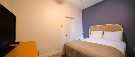 A bedroom with a bed, a television on a stand, and a door.