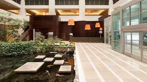 Un moderno vestíbulo de hotel con un estanque de peces koi, escalones de piedra y una recepción.