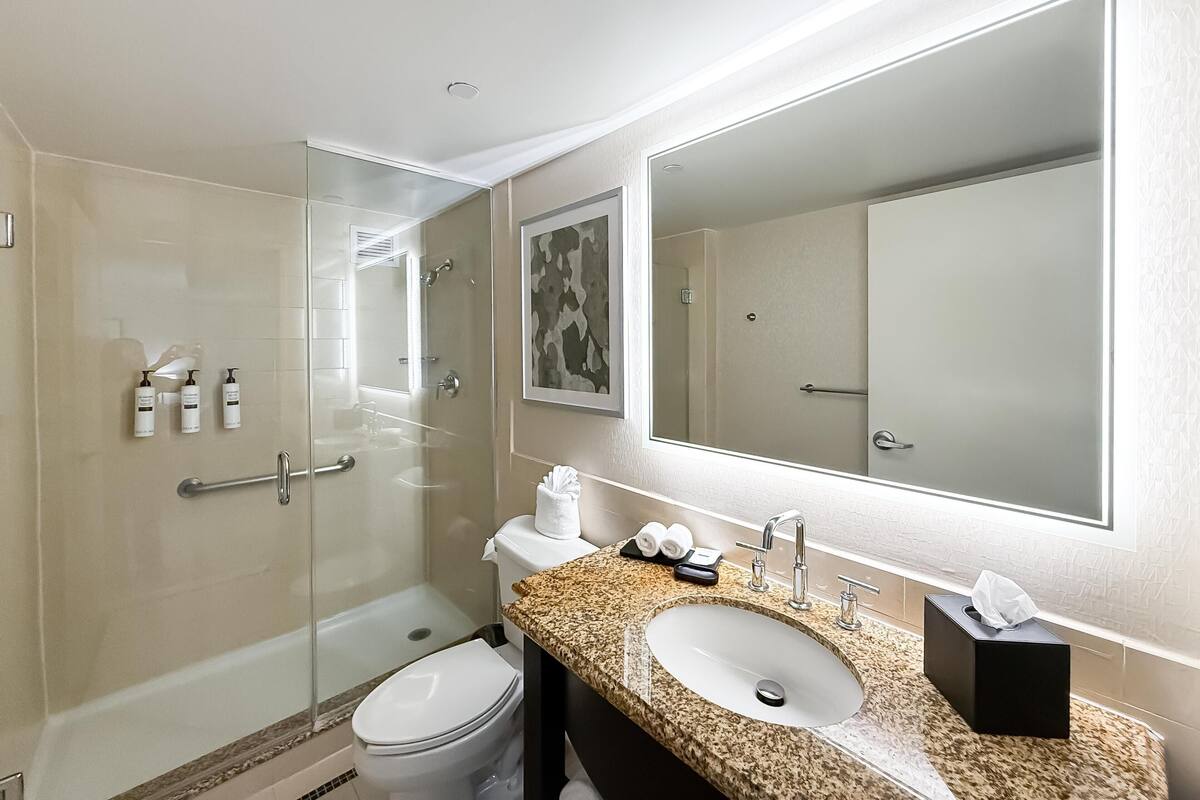 Une salle de bain moderne avec une douche à parois de verre, un lavabo doté d’un plan de travail en marbre et un grand miroir.