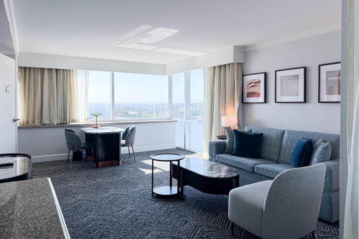 Een hotelkamer met een zithoek, een bank, een bijzettafeltje en uitzicht op de stad.