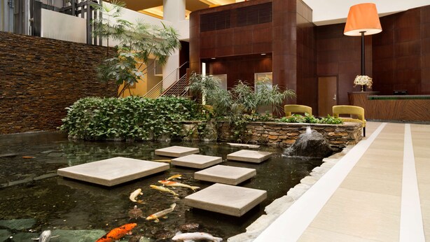 Un vestíbulo moderno con estanque de peces koi, escalones de piedra y plantas de interior.