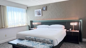 A hotel room with a bed, bedside lamps, a bench, a window with curtains, and a picture on the wall.