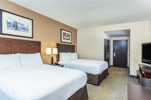 Quarto de hotel com duas camas, uma escrivaninha com televisão e quadros nas paredes.