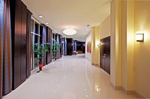 Un pasillo de hotel con piso de baldosas brillantes, ventanas amplias y plantas en macetas.
