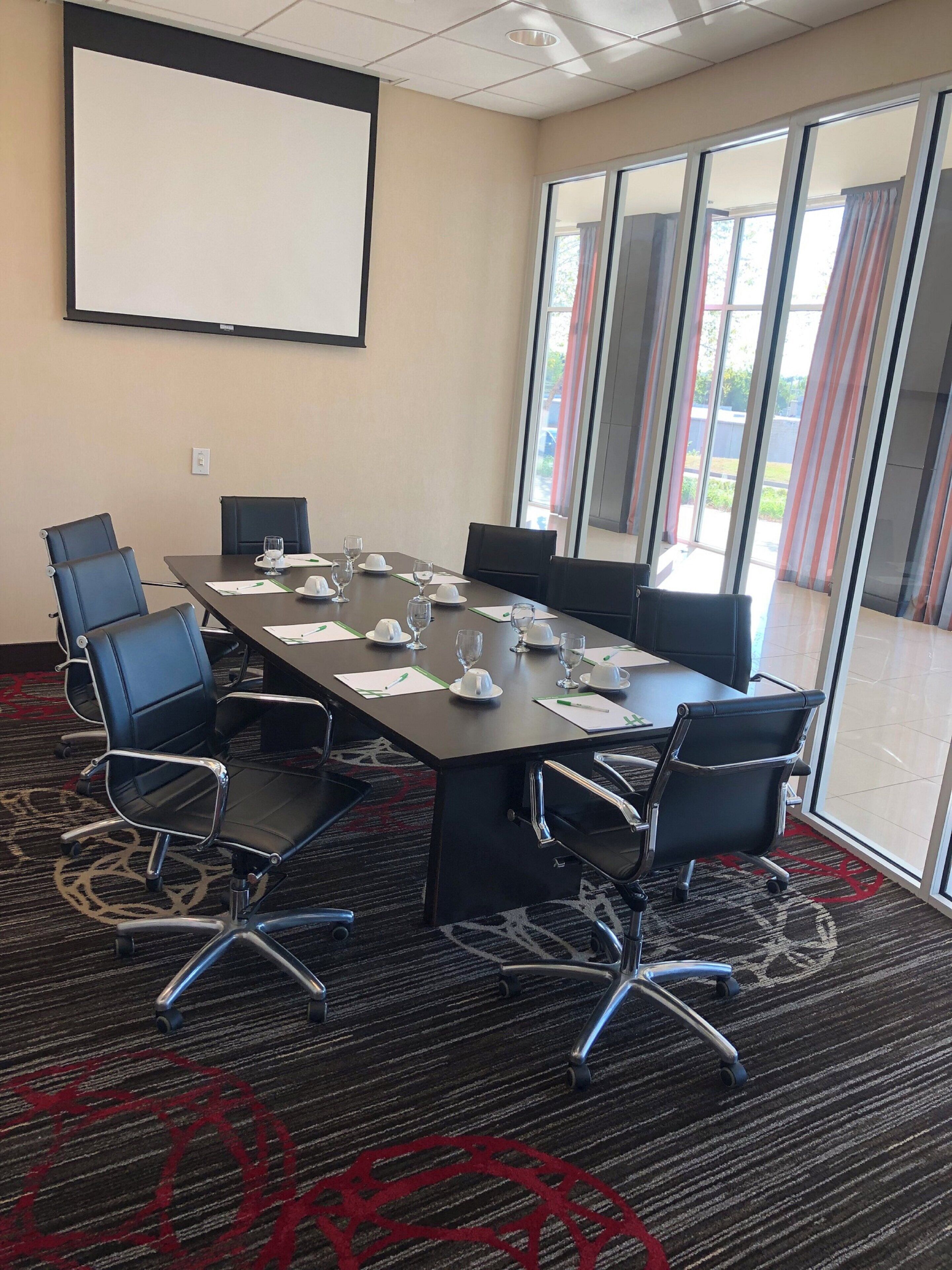 Ein Konferenzraum mit großem Tisch, Stühlen, einer Projektionsleinwand und Blick ins Freie durch große Fenster.