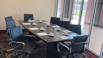 Un salón de conferencias con una gran mesa, sillas, una pantalla de proyector y vistas al exterior a través de amplias ventanas.