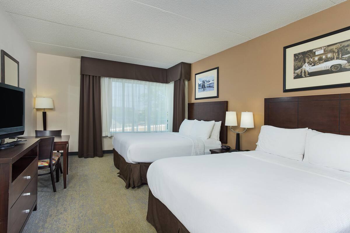 A hotel room with two beds, a desk with a TV, a chair, and a window with curtains.