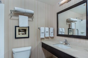 Casa de banho com papel de parede listrado, sanita, lavatório com espelho e várias toalhas numa estante.