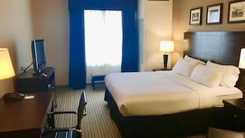 Una habitación de hotel con cama, escritorio, silla, lámpara y ventana con cortinas.