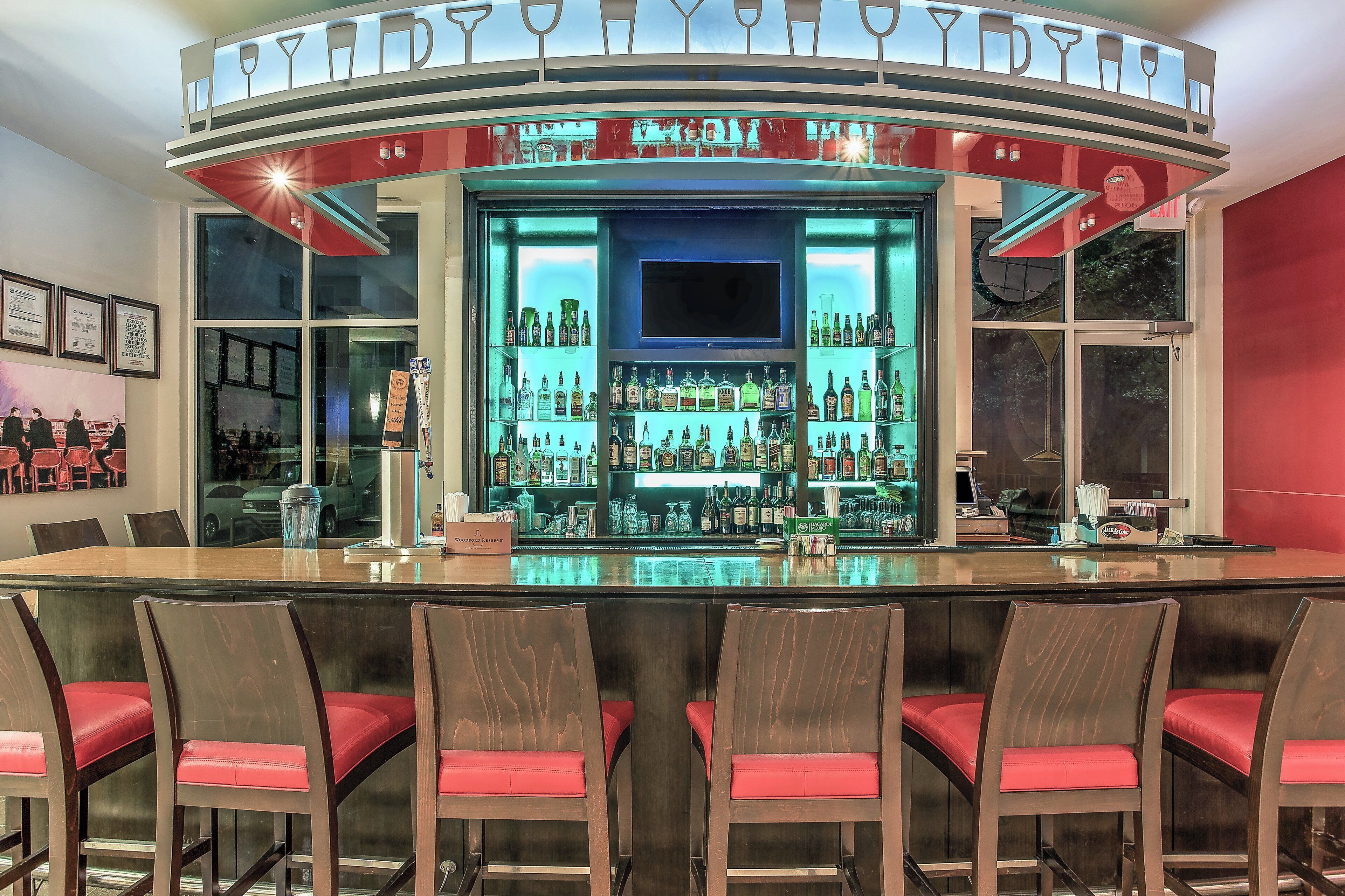 A bar area with a curved counter, multiple shelves of bottles, and red cushioned chairs.
