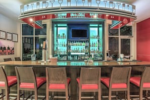 A bar area with a curved counter, multiple shelves of bottles, and red cushioned chairs. - Holiday Inn Louisville Airport - Fair/Expo by IHG (Louisville)