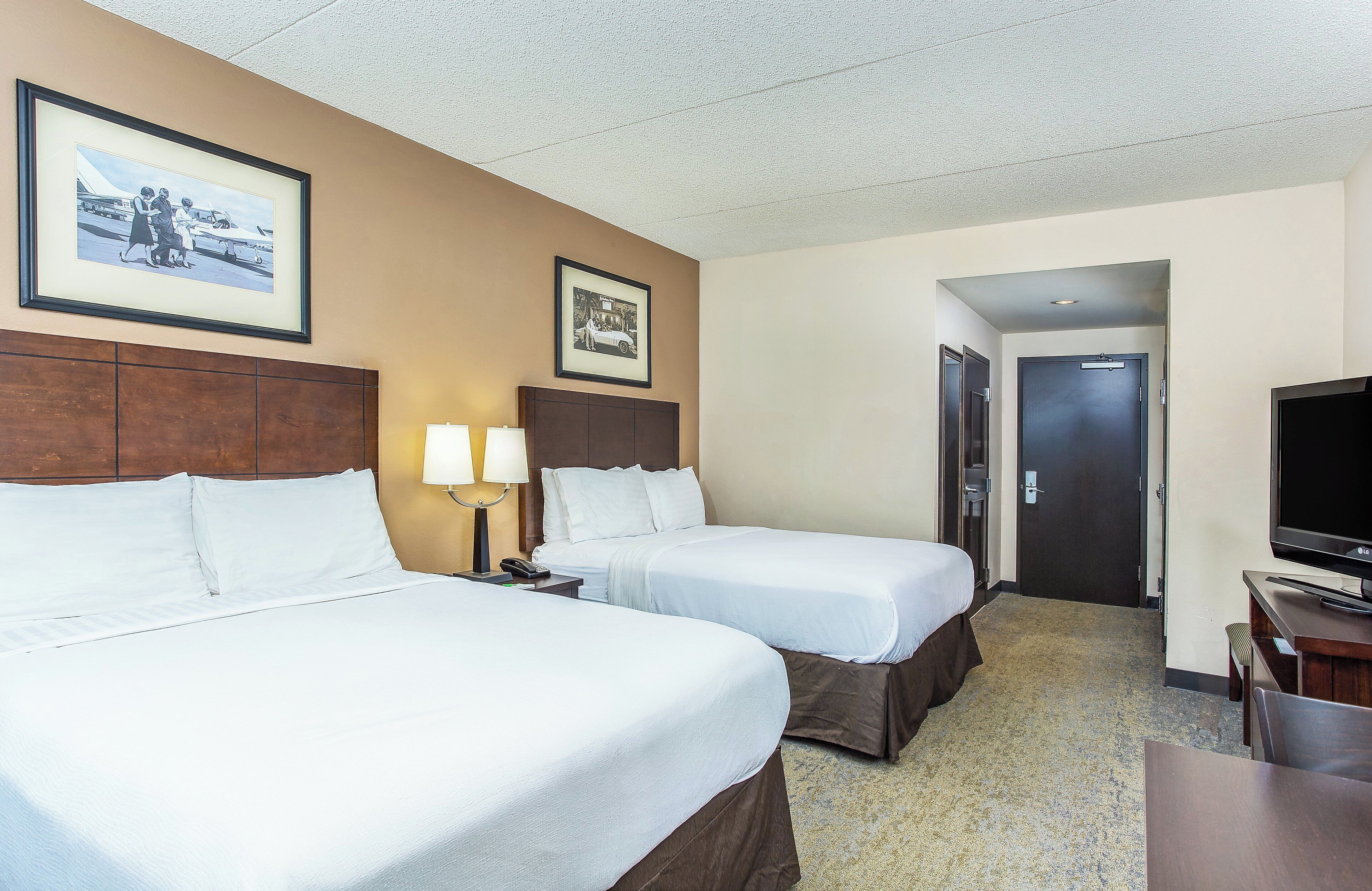 A hotel room with two beds, a desk with a TV, and framed pictures on the wall.