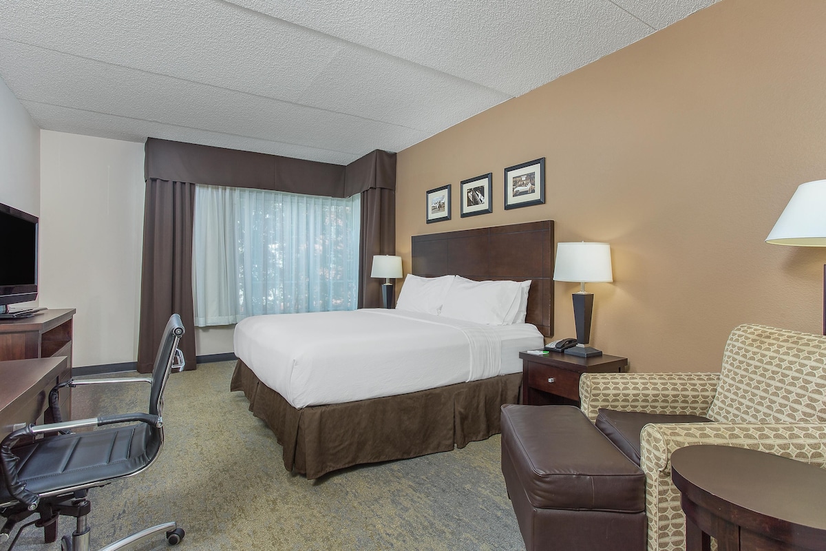 A hotel room with a bed, a desk, a chair, a sofa, and a TV.