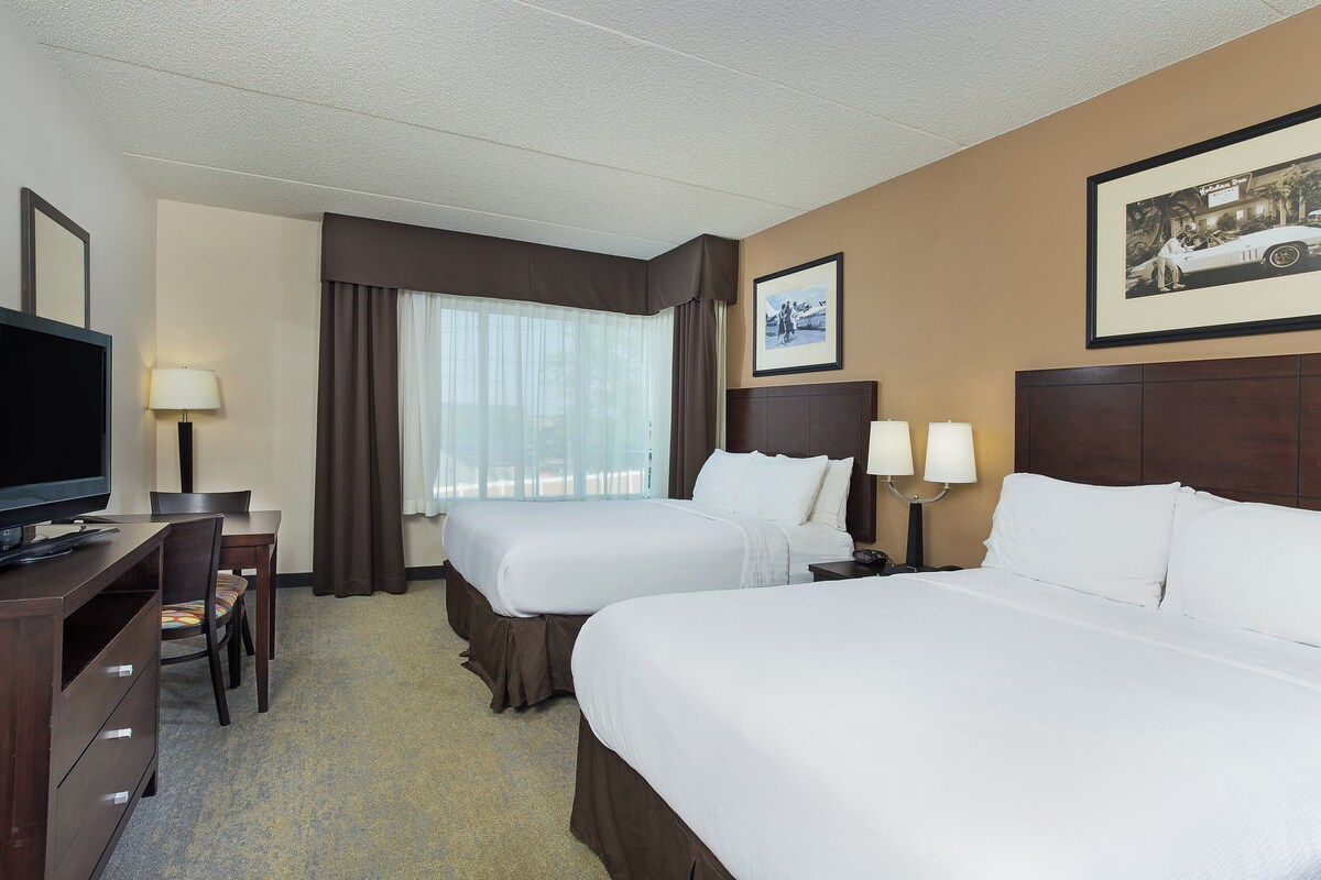 A hotel room with two beds, a desk, a television, and a window with curtains.